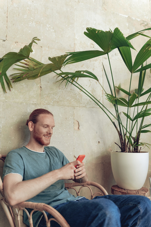 Relaxed bearded man is having fun with smartphone in cafeの写真素材