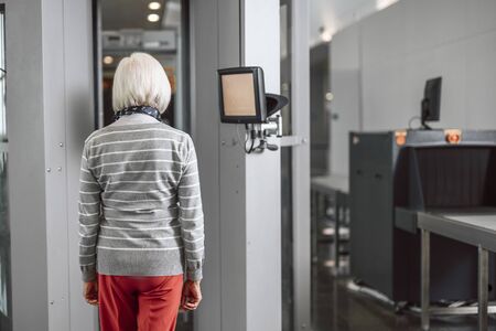 Old woman passing control at the airport through scanner