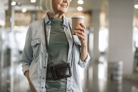 Happy old woman staying in hall with coffeeの写真素材