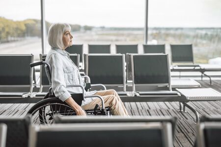 Cheerful mature woman on disabled carriage near panoramic windowsの写真素材