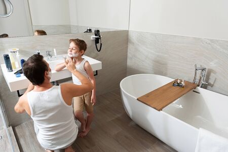 Dad and son are standing in the bathroom and shaving togetherの写真素材
