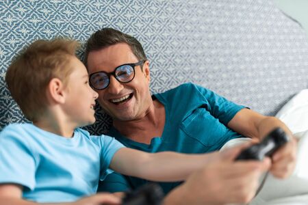 Smiling father and little son are playing the console together