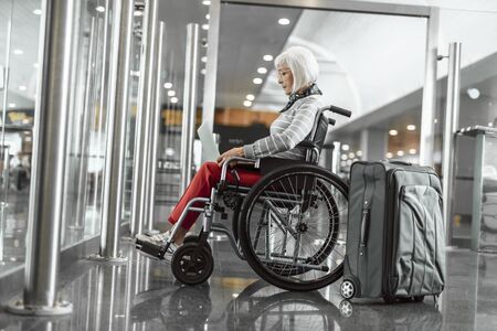 Cheerful mature lady on disabled carriage working at laptopの写真素材