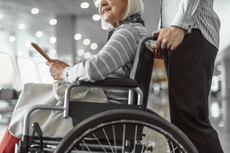 Female worker of airport holding wheelchair with elderly ladyの写真素材