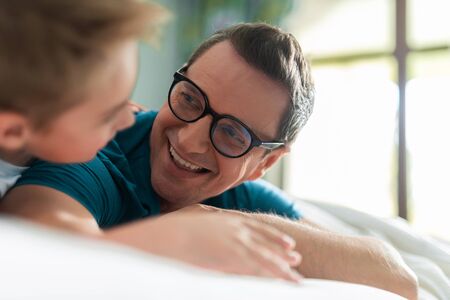Smiling father and son looking each other in bed at home
