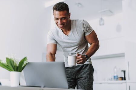 Happy man is starting morning with laptop and coffee indoorsの写真素材