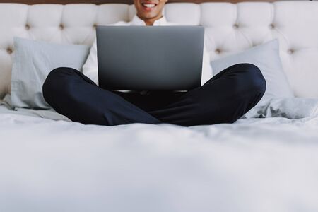 Jolly guy is using laptop in bedroomの写真素材