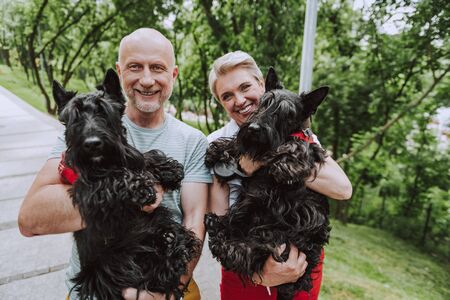 Smiling adult couple holding two black dogs in park