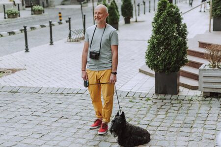 Smiling gray-haired man walking with black scotch terrier