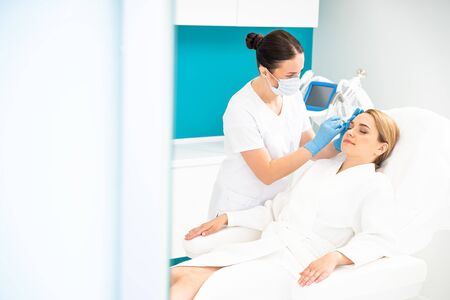 Caucasian beautician giving her client a shot in cosmetology clinicの写真素材