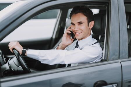 Happy young man sitting in his auto with smartphoneの写真素材