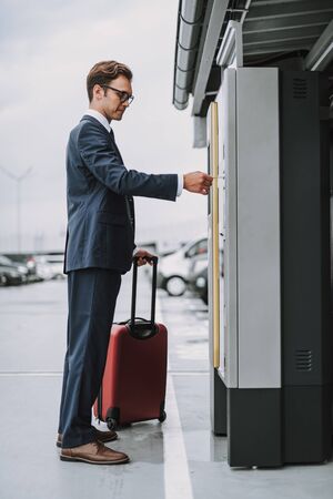 Young man in glasses making payment in the parking meter outdoorsの写真素材