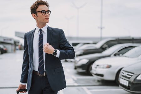 Young man wearing glasses while walking on the parking lot outdoorsの写真素材