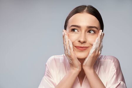 Charming young woman washing face with foaming cleanserの写真素材