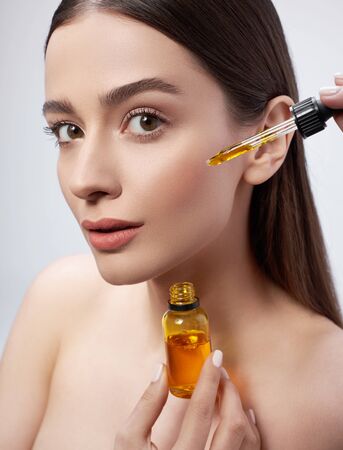 Beautiful young woman with perfect skin applying vitamin serum on her face