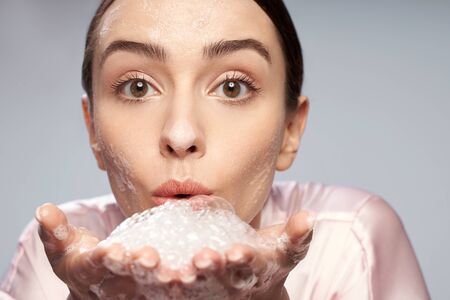 Beautiful young woman blowing foam while washing faceの写真素材