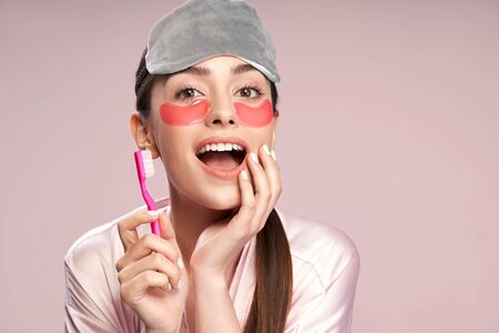 Charming girl with under-eyes patches holding toothbrush and touching her faceの写真素材