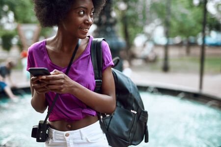 Smiling young afro-american lady with smartphone in the cityの写真素材