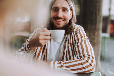 Joyful young man holding white cup of coffeeの写真素材