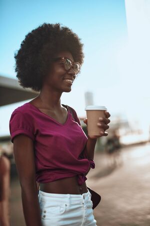 Smiling afro-american woman enjoying coffee on the streetの写真素材