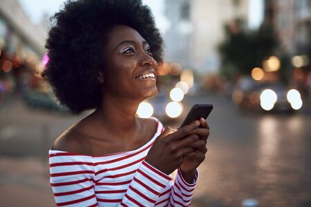 Happy young female is using smartphone outdoorsの写真素材