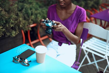 Calm afro-american woman holding camera in cafe outdoors