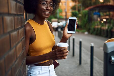 Joyful afro-american lady in glasses is holding smartphoneの写真素材