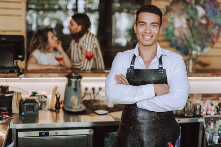 Handsome bartender in black apron standing in cafeの写真素材