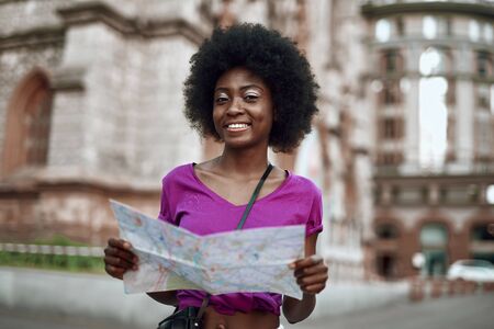 Smiling young woman standing on street with map