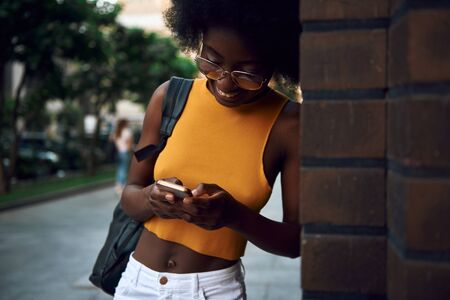 Pretty young afro-american woman typing message outdoorsの写真素材
