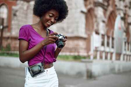 Smiling young afro-american woman using retro camera on the streetの写真素材