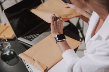 Cropped photo of Caucasian lady working at laptop. Female model sitting at table and looking at smartwatchの写真素材