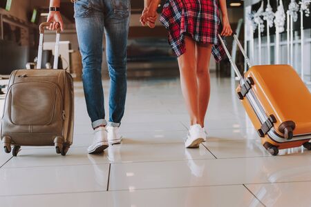Caring man and woman are carrying suitcases on their way to plane. They are feeling happy anf holding each other handの写真素材