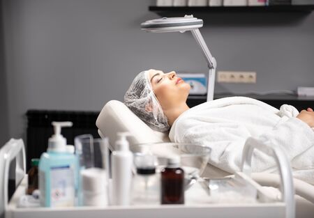 Serene young woman in disposable medical cap relaxing at beauty salonの写真素材