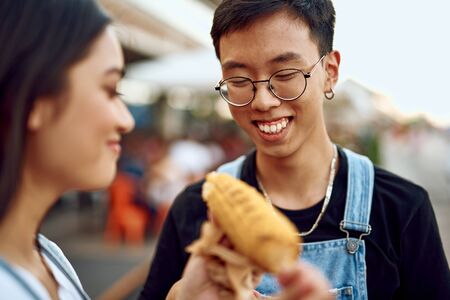 Happy asian guy and lady eating sweet grill corn
