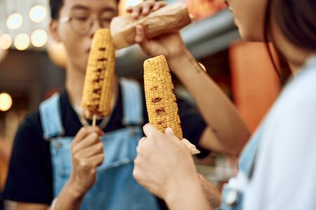 Asian couple eating sweet grill corn outdoorの写真素材