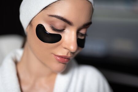 Charming young woman using black under-eye patches