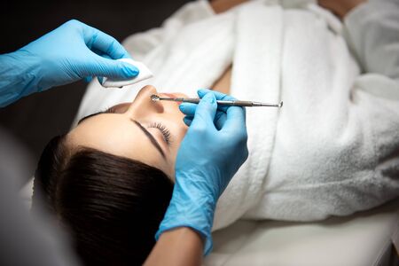 Beautician in sterile gloves using blackhead remover for cleaning lady faceの写真素材