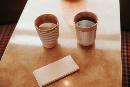 Close up top angle picture of two cup with hot beverage staying on table and mobile phone besideの写真素材