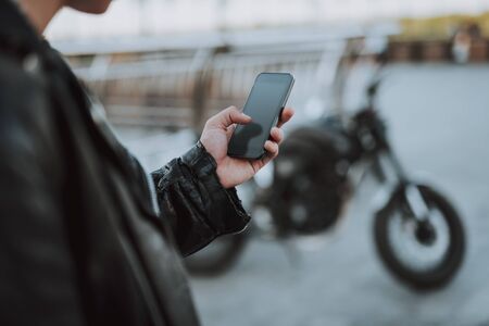 Man in leather jacket using modern smartphone. Motorbike on the backgroundの写真素材