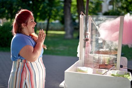 Young and fat woman looking at cotton candy machine