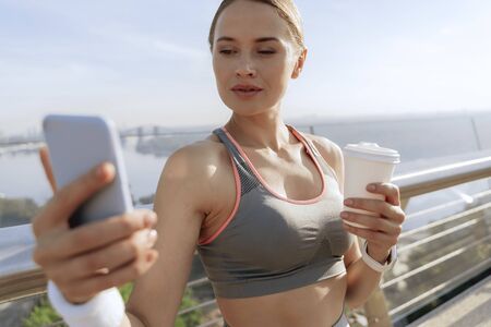 Athletic female with coffee looking at smartphone