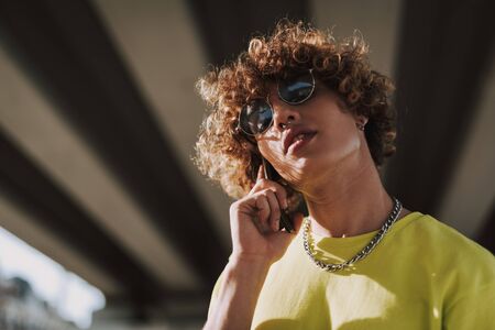 Calm curly young man in sunglasses talking on the phone