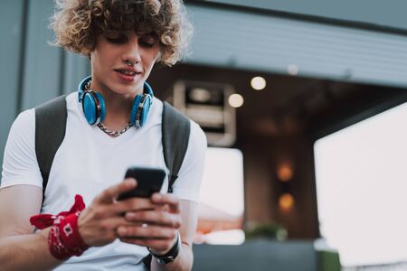 Curly student looking at the screen of smartphoneの写真素材