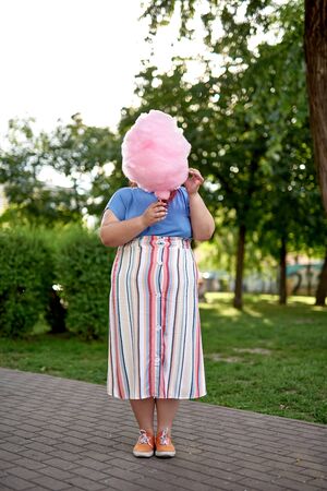 Young fat woman covering face with cotton candy