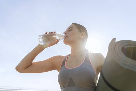 Young lady with roll mat drinking clean water