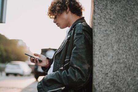 Calm man by the wall using smartphone