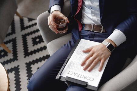 Businessman holding whisky while sitting with contract