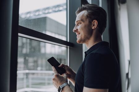 Smiling man looking into the window while holding smartphone