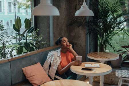 Young afro-american woman sitting in cafe with beverage